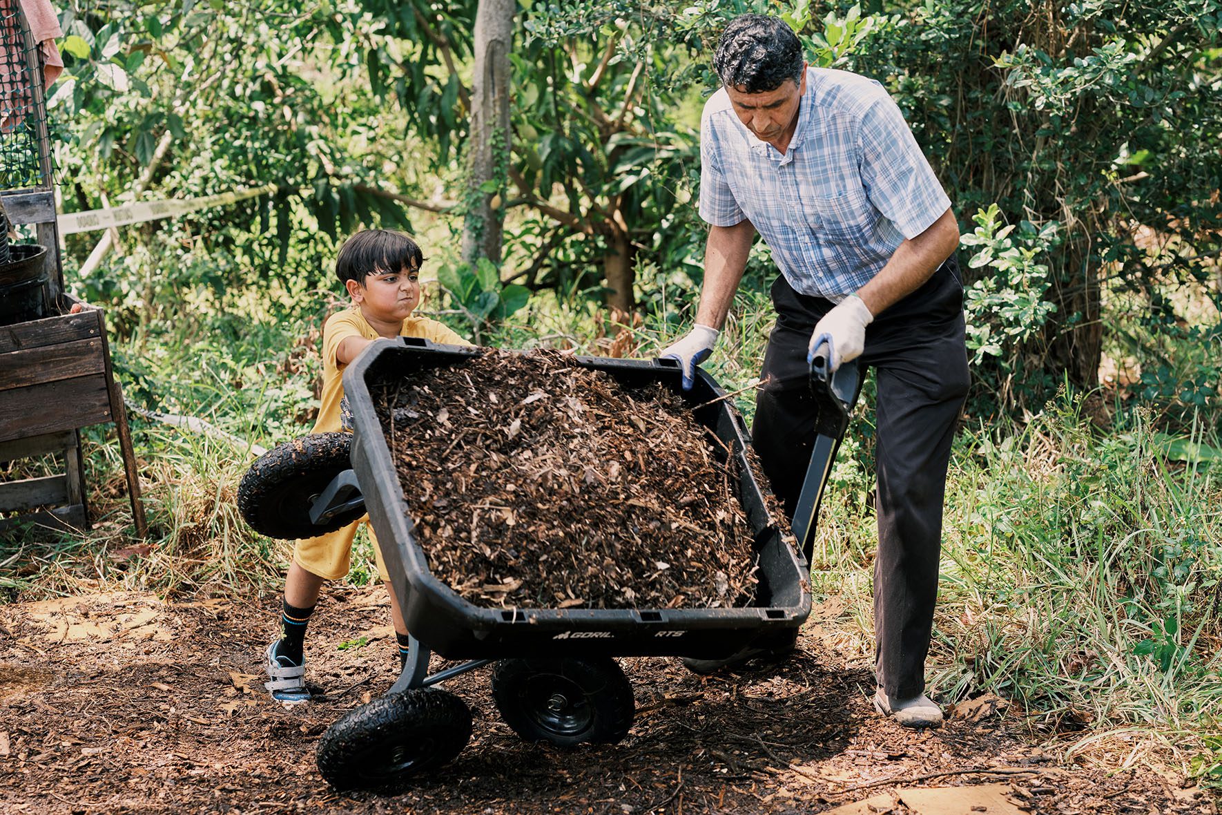Rahmatullah Hamkar and Zekkra Sayed Jan, 10, lay down fresh soil as they work to expand the Refugee Garden in Clearwater, Florida on June 1, 2023. | Community Garden for Refugees Offers Belonging & a Taste of Home | HIAS