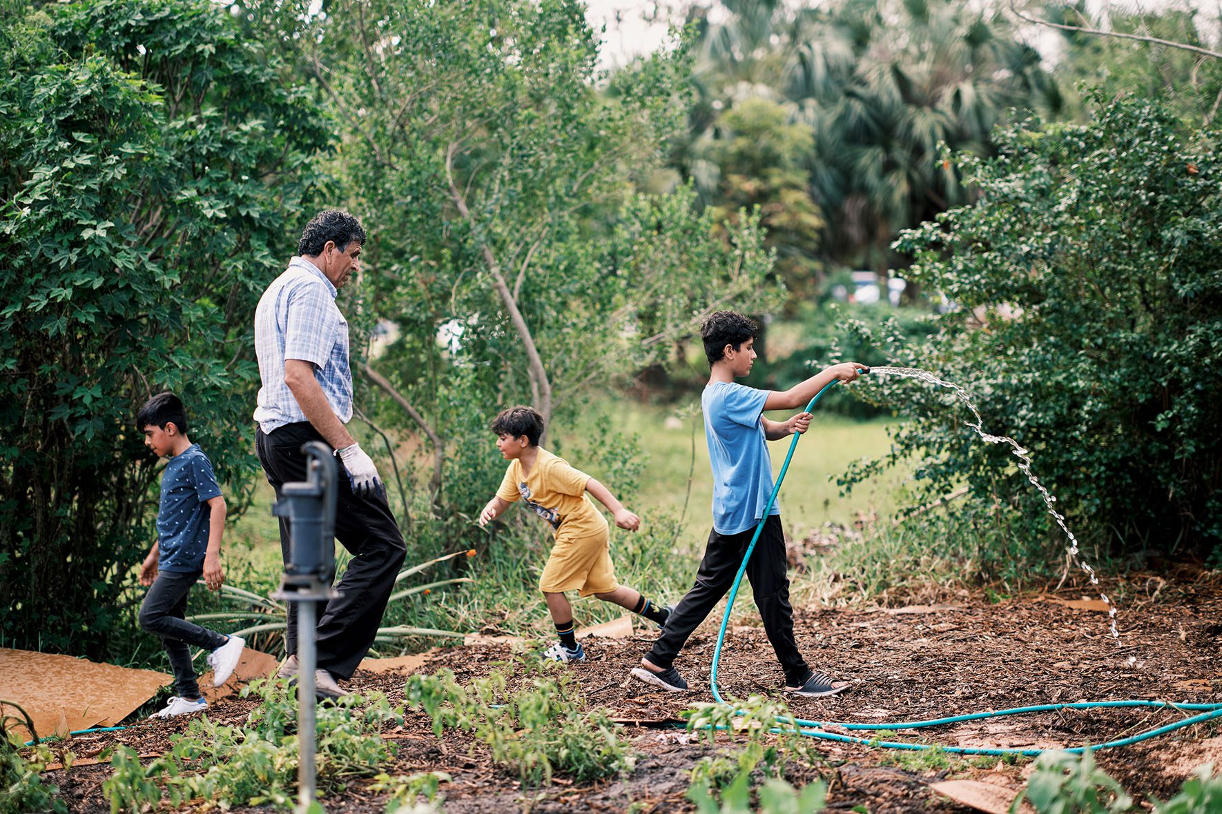 Rahmatullah Hamkar, 51; Zekkra Sayed Jan, 10; and Omar Hamkar, 9; at work and at play in the Refugee Garden in Clearwater, Florida on June 1, 2023. | Community Garden for Refugees Offers Belonging & a Taste of Home | HIAS