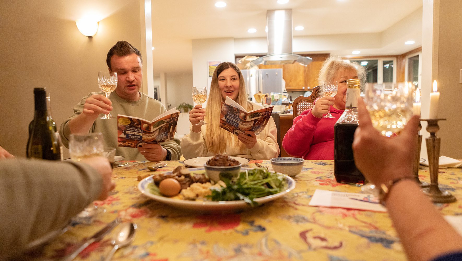 Members of the Levit/Kushnarov family, who fled Ukraine and were resettled in the U.S. by a HIAS Welcome Circle, raise their wine glasses while reading from the Haggadah during a Passover Seder with members of their Welcome Circle in Portland, Oregon. | Jewish Ritual Centering Refugees