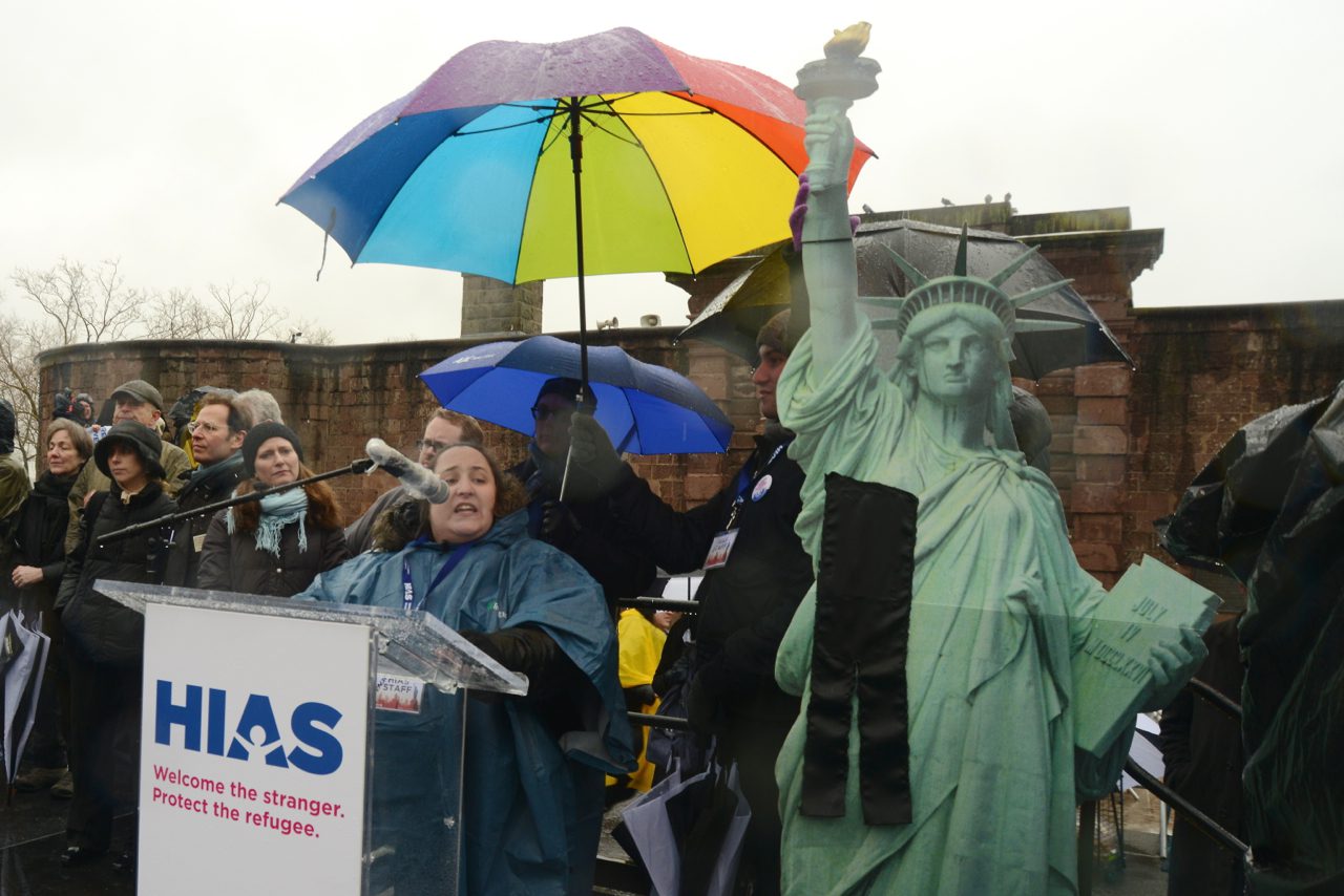Rabbi Rachel Grant Meyer, Director of Education at HIAS, the global Jewish nonprofit that protects refugees, leads a 'minyan' of leaders from New Yorks Jewish community during the symbolic 'kriah' Jewish ritual, mourning the loss of lives of refugees, as part of the Jewish Rally for Refugees in Battery Park, New York, on February 12, 2017. A kriah ribbon was affixed to a cardboard cutout of the Statue of Liberty on stage. The gathering was one of several rallies nationwide convened by HIAS and co-sponsored by Jewish organizations. (Photo: Gili Getz/HIAS)