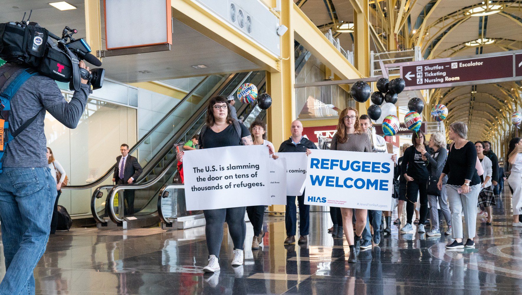 Media films a group of activists from HIAS and partner organizations as they demonstrate against the Trump Administration's ban on refugee admissions at Ronald Reagan Airport in Washington, D.C. on October 16, 2019. (Eric Kruszewski for HIAS)