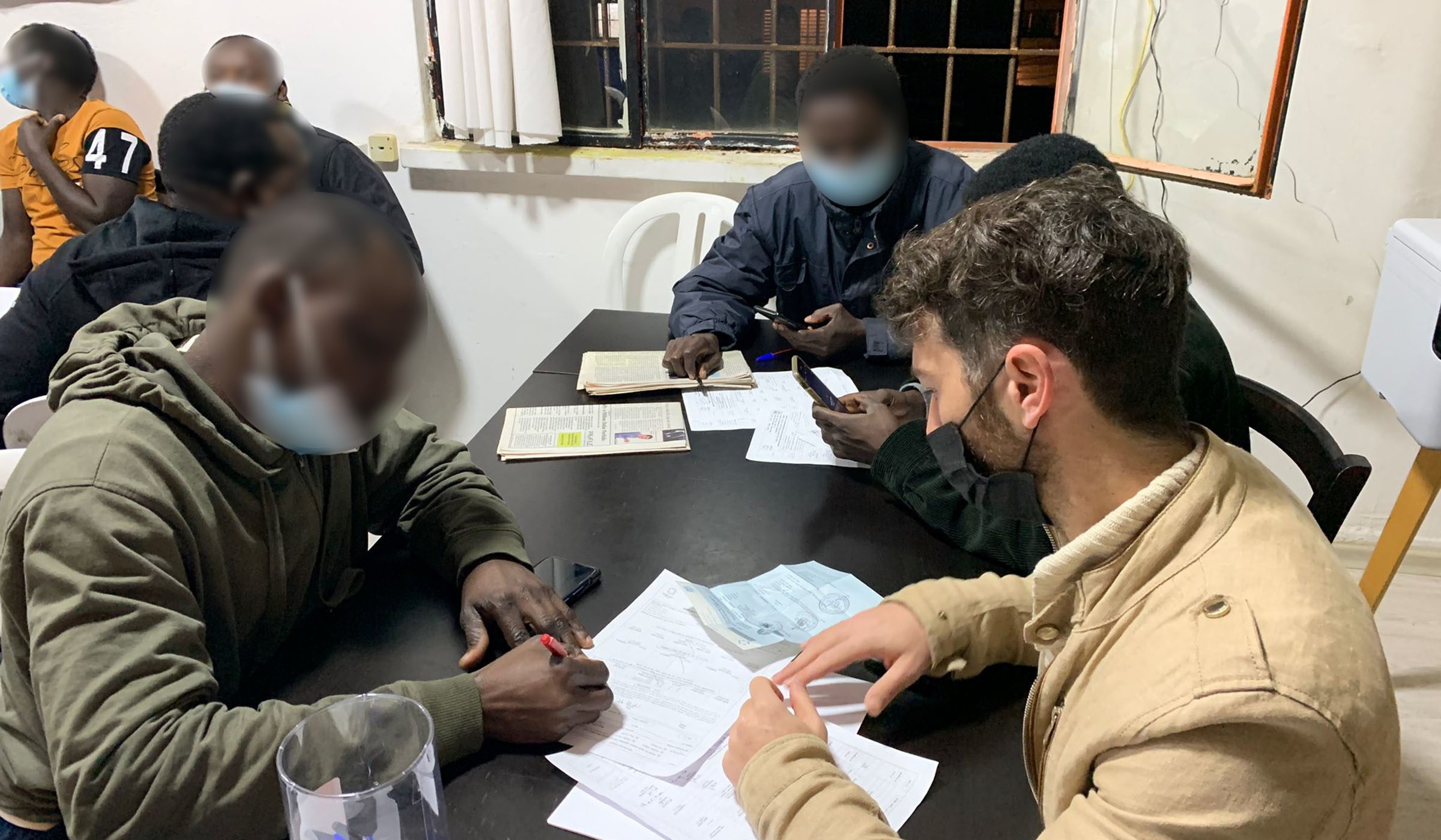 HIAS Israel's deputy director Nimrod Avigal (R) helps a Sudanese asylum seeker fill out forms to get temporary residency status. January 2021. (HIAS Israel)