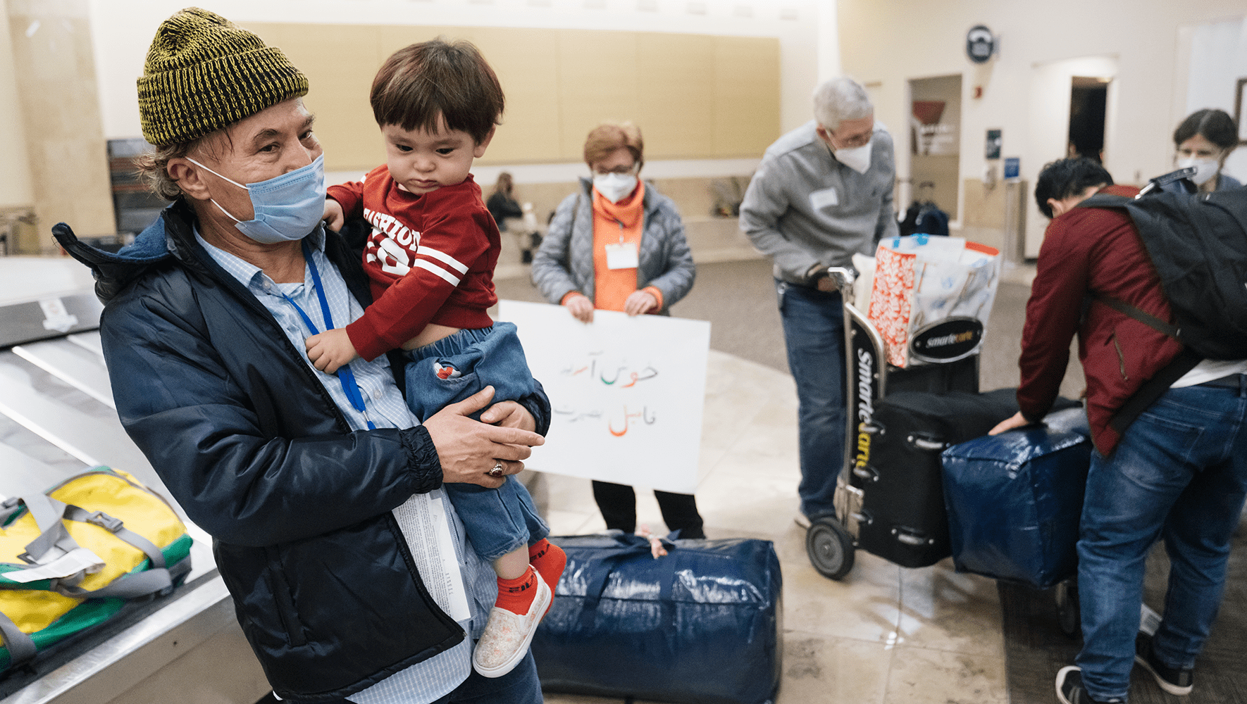 An Afghan man and his son after arrival at the baggage claim of John Wanye Airport in Orange County, Feb 19, 2022. They were greeted by a group of Welcome Circle volunteers. (Eric Thayer for HIAS)