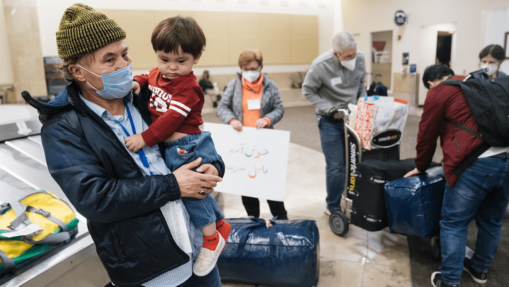 Un hombre afgano y su hijo tras su llegada a la recogida de equipajes del aeropuerto John Wanye, en el condado de Orange, el 19 de febrero de 2022. Fueron recibidos por un grupo de voluntarios del Círculo de Bienvenida. (Eric Thayer para HIAS)