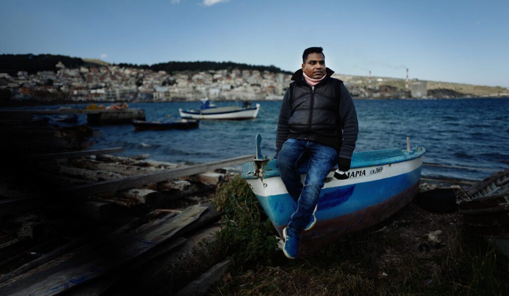 A man sits on the edge of a docked boat on the shore of the Greek island of Lesvos.