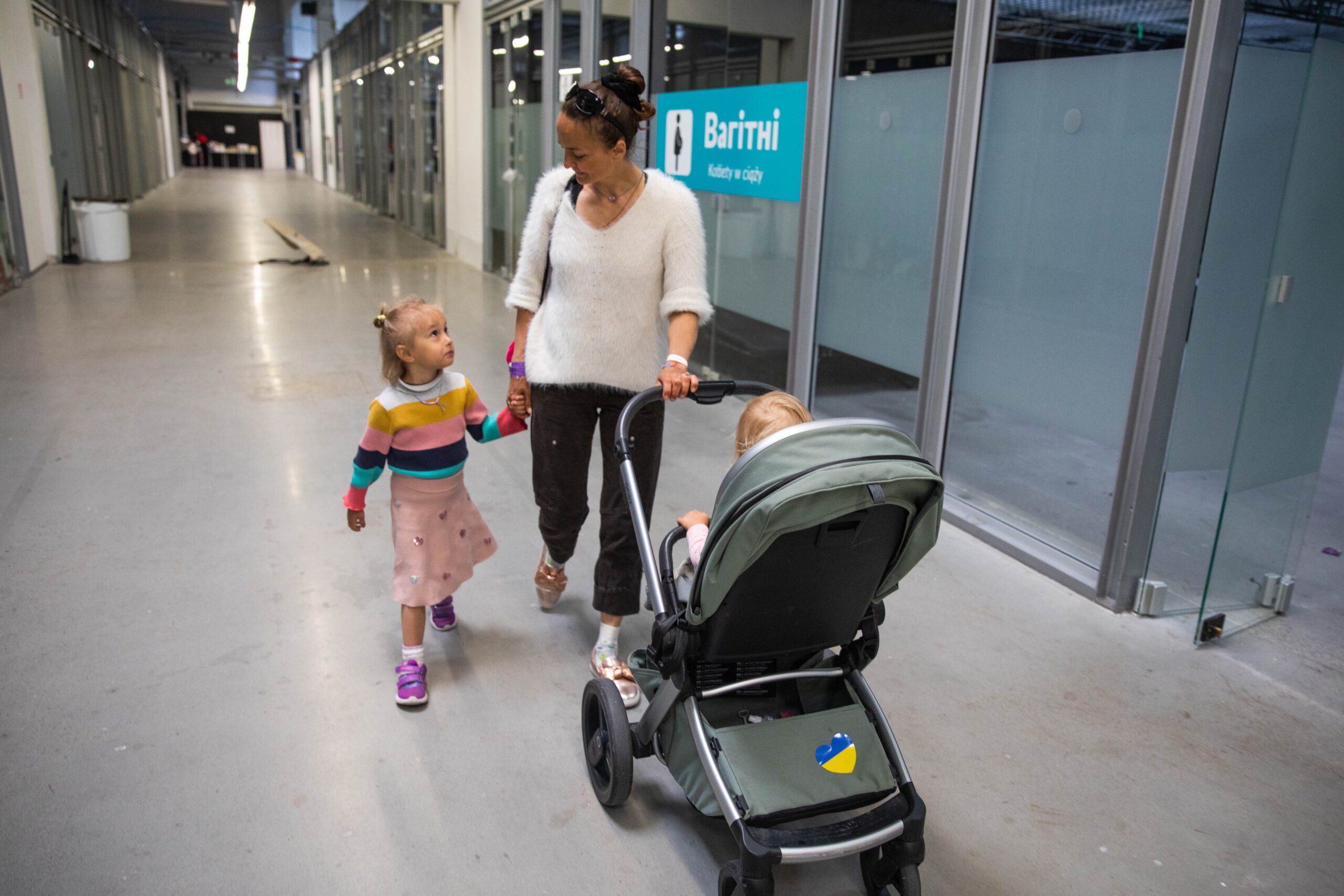 Mariia Radionova and her daughters Lada and Rada walk through a hallway in a temporary housing center for refugees from Ukraine in Ptak Warsaw Expo on May 26, 2022 in Nadaryzn, Poland.