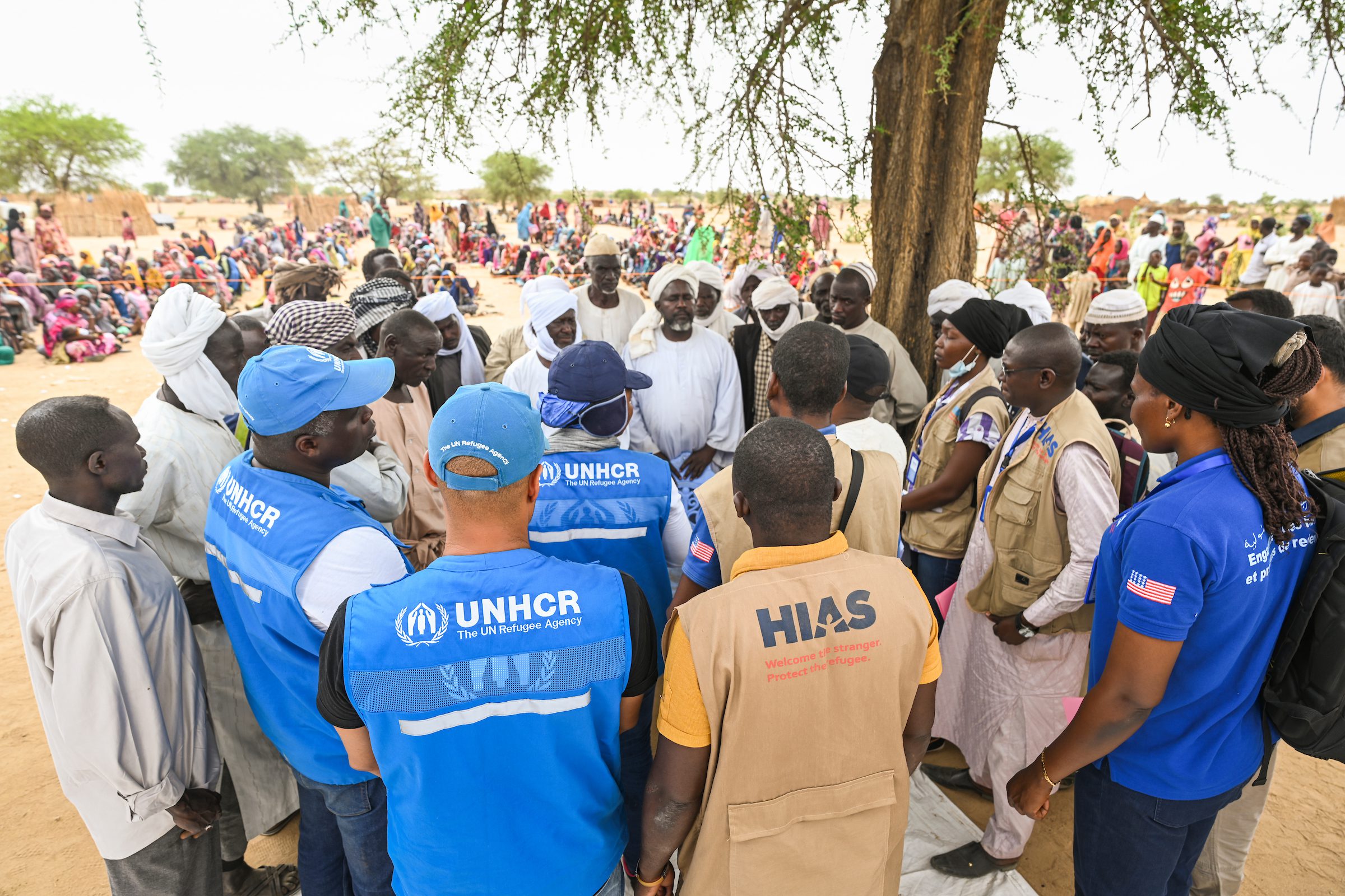 Aid workers talking to Sudanese refugee leaders outside under a tree