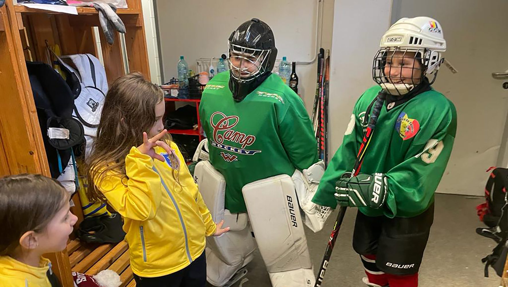 Kids in green hockey jerseys and full ice hokey uniforms smile in locker room