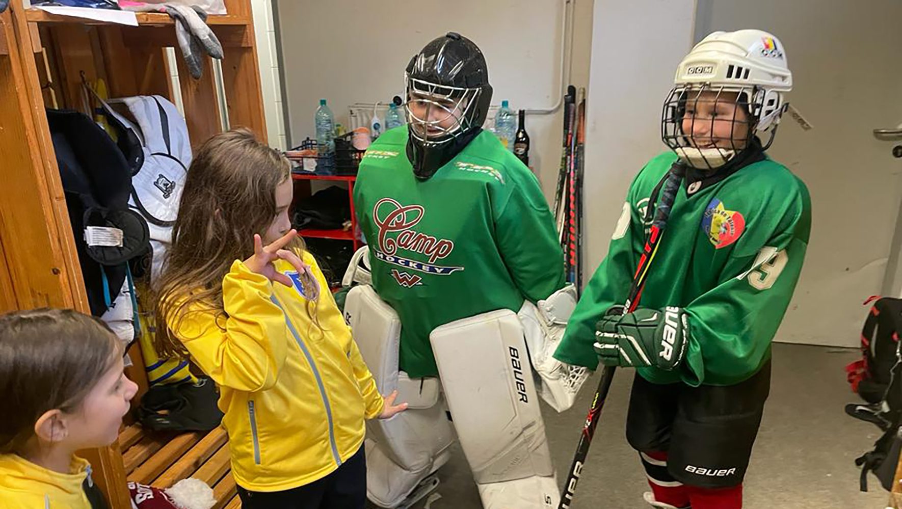 Chicos con camisetas verdes de hockey y uniformes completos de hokey sobre hielo sonríen en los vestuarios