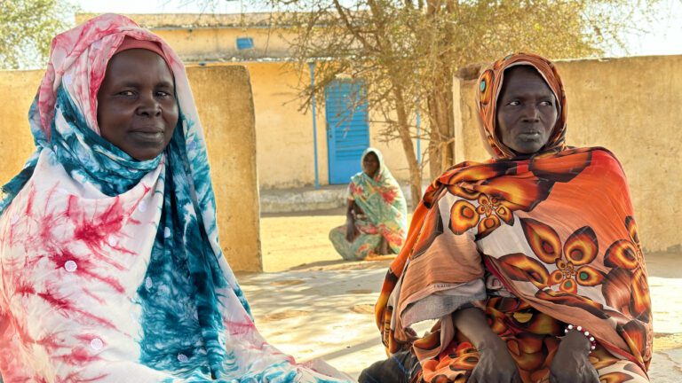 Two women sit at a refugee camp in Chad.