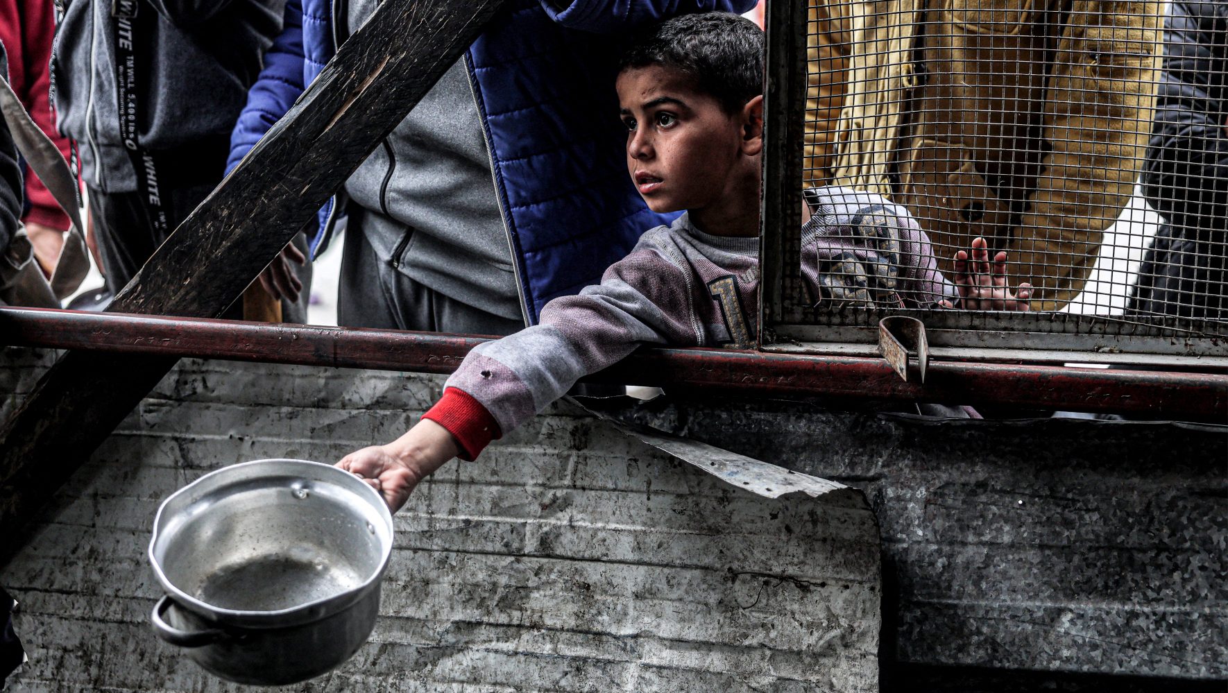 Un niño sostiene una olla vacía mientras espera junto a otros palestinos desplazados en la cola para recibir comidas proporcionadas por una organización benéfica antes de la ruptura del ayuno. 
