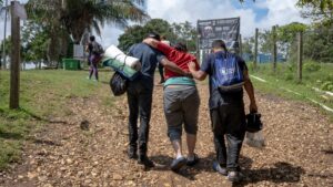 Two migrants help a limping woman.