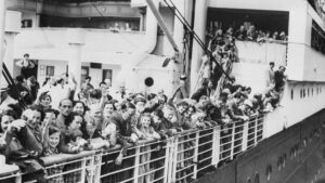 Jewish refugees aboard the MS St. Louis crowd along the ship’s railing, some waving and smiling, as the ship departs Hamburg in 1939 in a failed attempt to find refuge from Nazi persecution.