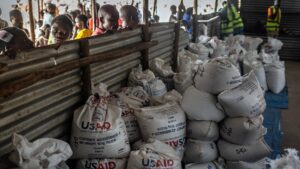Congolese refugees look through a corrugated metal fence at batches of food delivered by USAID.