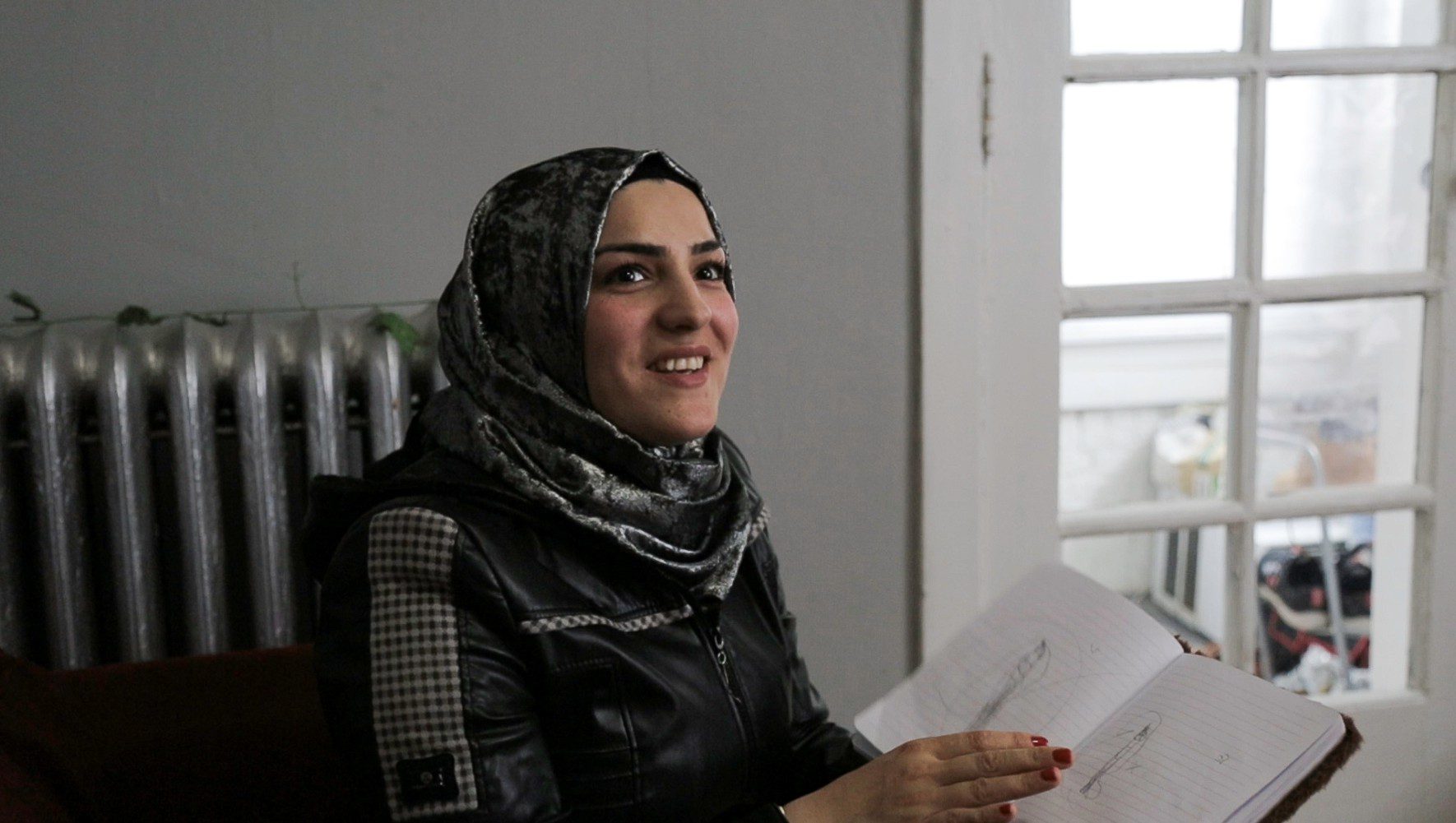Alaa, a Syrian refugee supported by community sponsorship, shows drawings by her daughter in their Chicago home in 2025. (Lindsay Kagalis/HIAS)