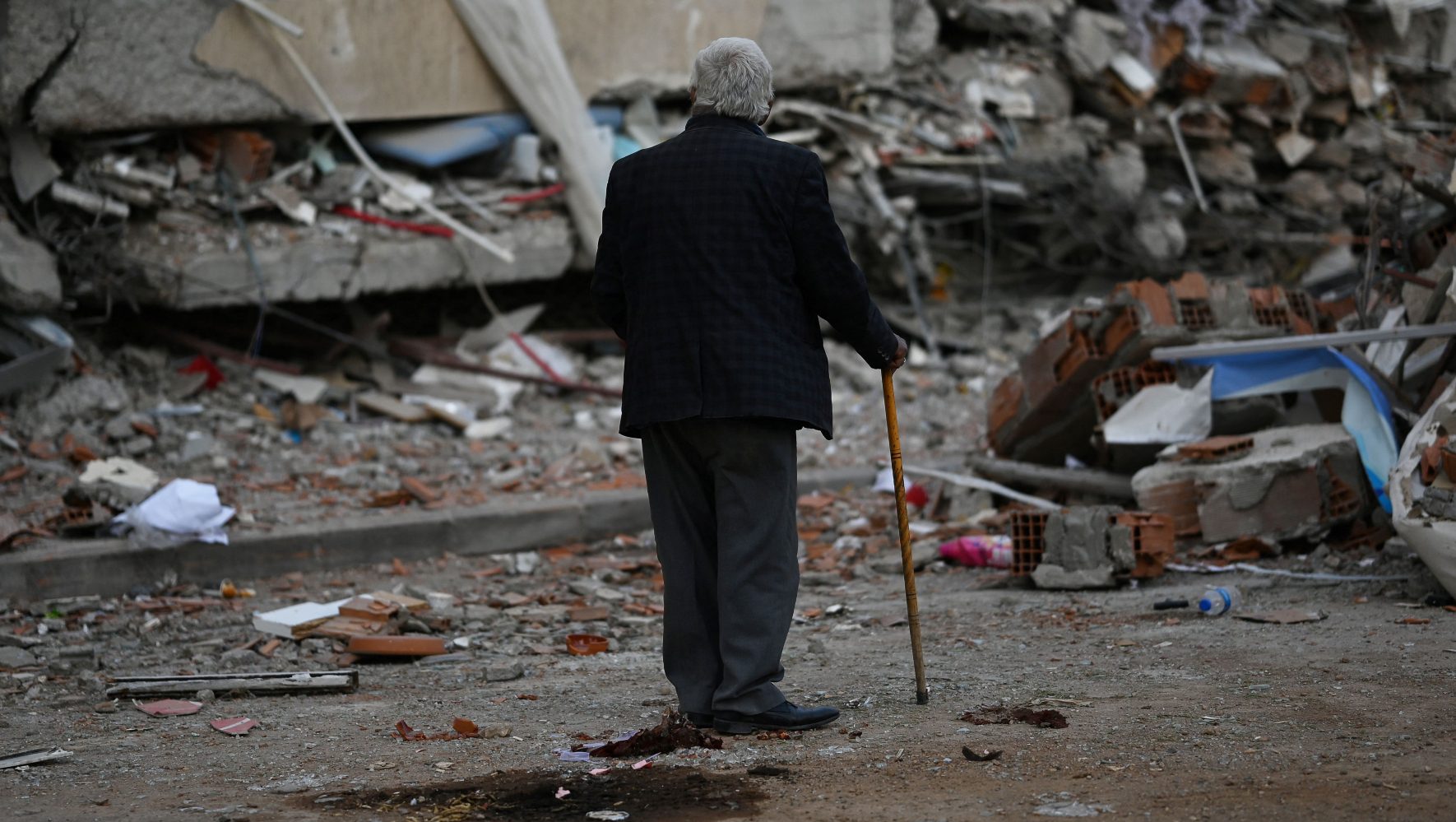 A victim of an earthquake in Turkey stands in front of rubble.