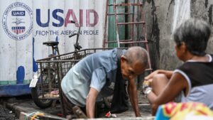 A man kneels in front of a container with the USAID logo painted on it.