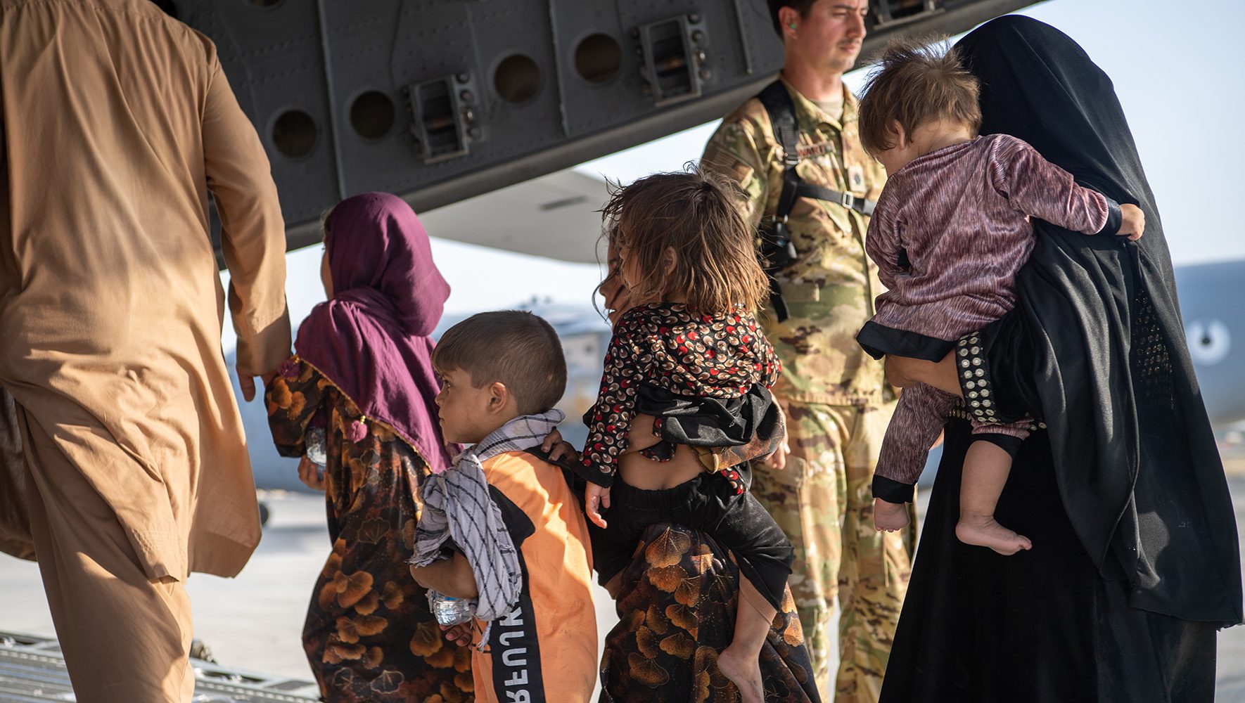 Pilotos y encargados de carga de las Fuerzas Aéreas estadounidenses ayudan a los pasajeros a subir a un avión durante la evacuación de Afganistán. | Los solicitantes de asilo afganos luchan por obtener un estatuto legal en Estados Unidos | HIAS