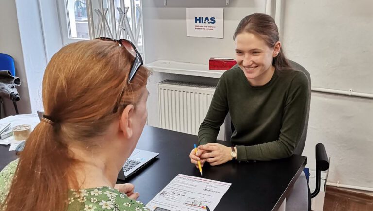 Woman smiling and helping woman with paperwork across a desk