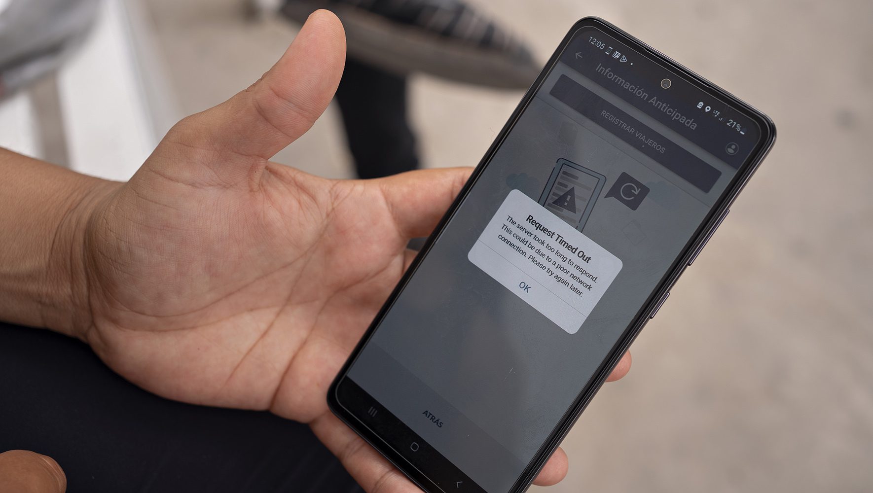 Una persona sostiene su teléfono móvil, mostrando un mensaje de error en la aplicación CBP One. El mensaje dice: