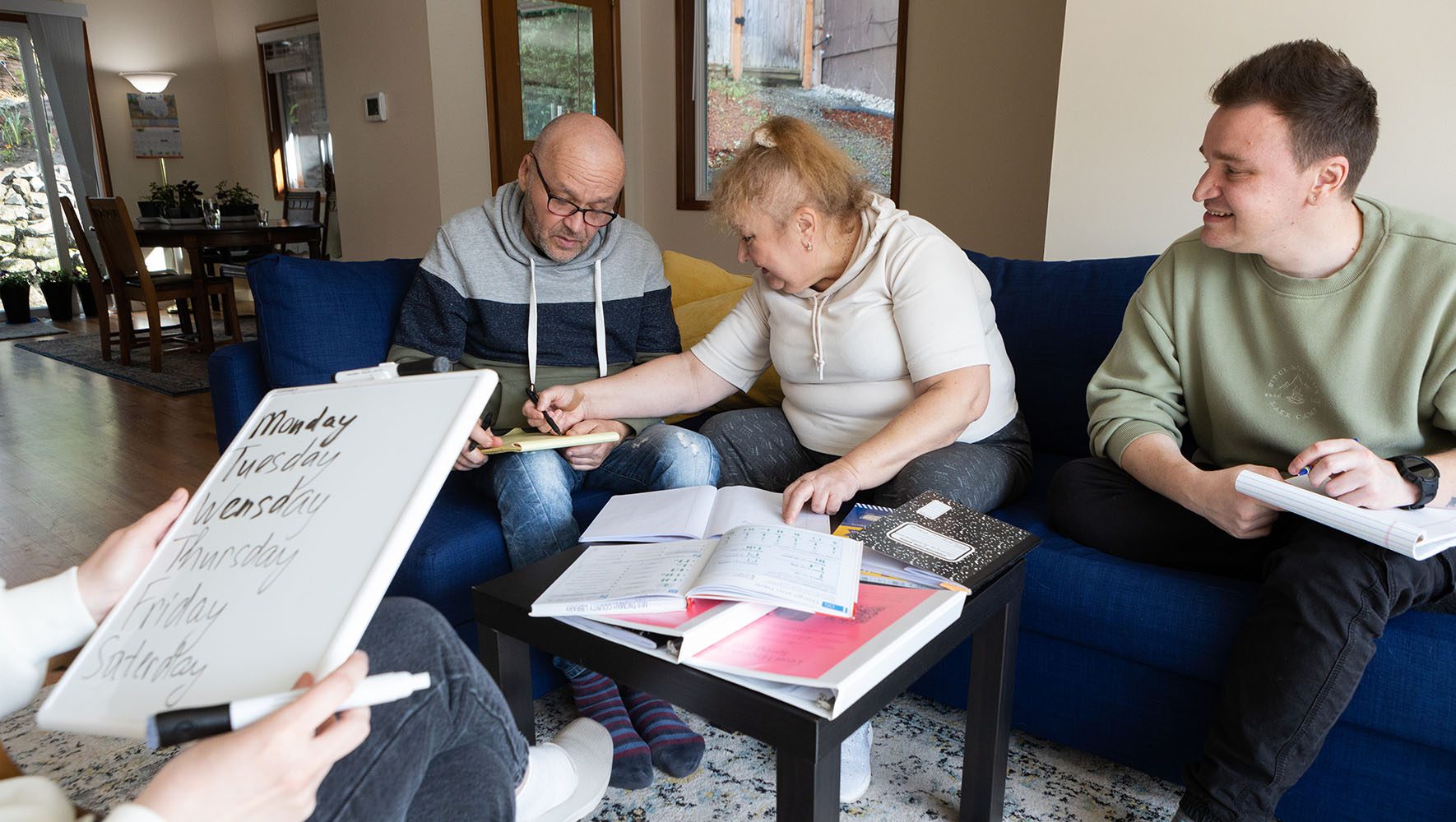 Tamila Kusharova, center, helps her husband Oleksandr with spelling days of the week in English during an impromptu English practice at their home.| In Time for Passover, Ukrainians Find Jewish Community in U.S. | HIAS