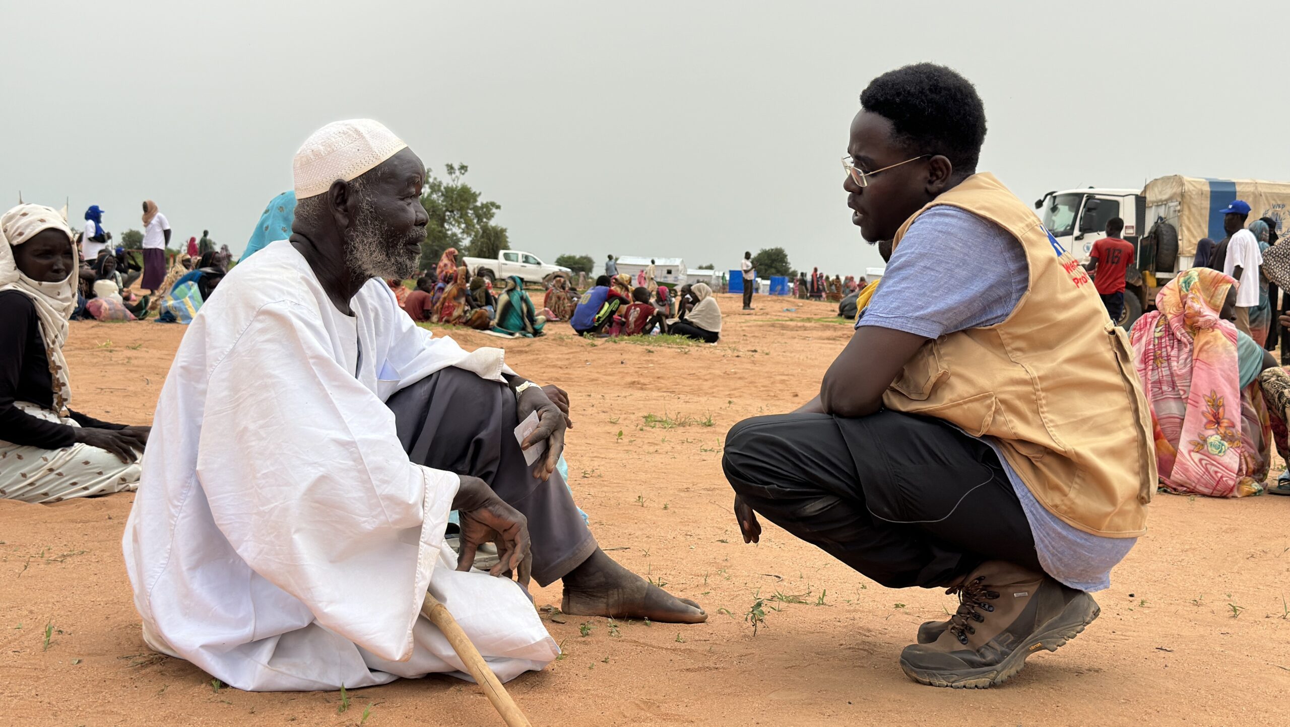 Man in white in desert speaking to man kneeling