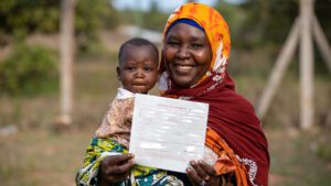 A Kenyan mother holding her young daughter happily displays her daughter's birth certificate. Birth certificates and other legal documentation are an important element in preventing a person from becoming stateless. | Statelessness | HIAS